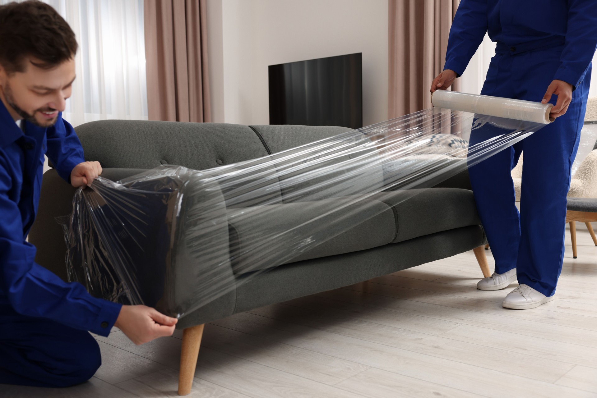 Male movers with stretch film wrapping sofa in house